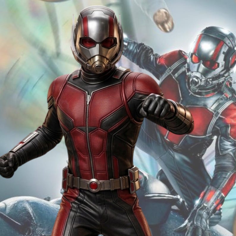 May include: A full-body shot of a person in a red and black Ant-Man costume. The costume features a silver helmet with red accents and a breathing apparatus. The suit has a zipper down the front and a utility belt. A second Ant-Man figure is in the background.