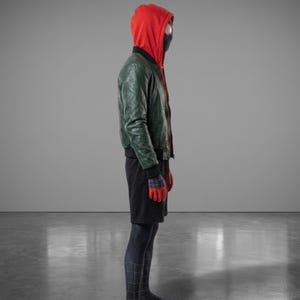 以下が含まれることがあります： 赤いフード付きスウェットシャツ、緑の革のジャケット、黒いショートパンツ、黒いマスクを特徴とするコスチューム。手袋は赤と青です。コスチュームはスーパーヒーローに似せてデザインされています。