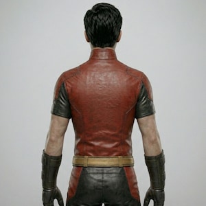 May include: A red and black leather jacket with a high collar and short sleeves. The jacket has a brown belt and is paired with black pants and gloves. The person is facing away from the camera.