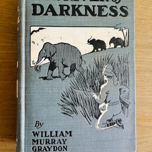 May include: Vintage book titled "The River of Darkness" with a light blue cover. The cover features illustrations of elephants, a person with a rifle, and the author's name, William Murray Graydon.