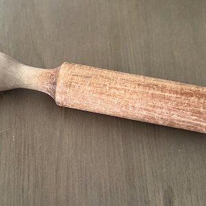 May include: A wooden rolling pin with a rounded handle and a cylindrical rolling surface. The rolling pin is made of light-colored wood and shows signs of wear. It is designed for use in baking and pastry making.