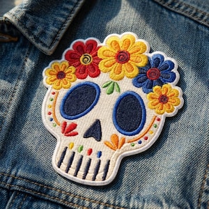 May include: An embroidered patch featuring a white skull adorned with a crown of vibrant yellow, red, and blue flowers. The skull has dark blue eye sockets, a triangular nose, and vertical black lines for teeth, with colorful accents along the jaw.