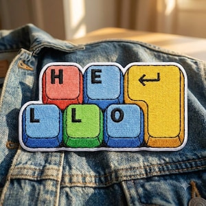 May include: An embroidered patch shaped like computer keyboard keys arranged to spell HELLO. The keys are red, blue, green, and yellow, with black letters and a black enter arrow symbol. The patch has a white border and is placed on denim fabric.