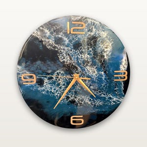 May include: A round wall clock featuring a glossy, abstract ocean wave design in shades of deep blue, black, and white. The clock face has gold-colored numerals at the 12, 3, 6, and 9 o'clock positions, with matching gold-colored clock hands.