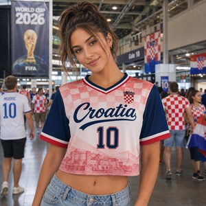 May include: A cropped Croatia soccer jersey featuring a red and white checkered pattern on the upper chest, dark blue sleeves with red and white trim, the word Croatia in blue script, the number 10 in blue, and a red graphic of a coastal city.