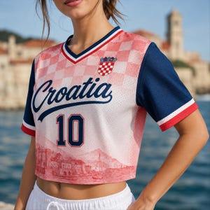 May include: A short-sleeved V-neck jersey featuring a red and white checkered pattern, the text Croatia, the number 10, and a small crest. The shirt has solid navy blue sleeves with red and white trim, and a red graphic of a coastal town.