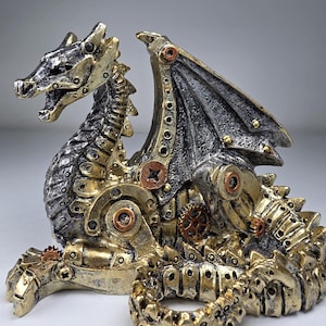 May include: A dragon figurine featuring a metallic gold and silver finish with mechanical details including visible gears, rivets, and circular plates integrated into its body, wings, and tail, presented in a seated, alert posture.