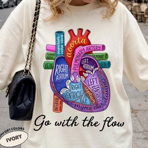 May include: Ivory t-shirt with a detailed anatomical heart diagram, including labels for aorta, atrium, and ventricle. The phrase "Go with the flow" is printed below. The shirt is from Comfort Colors.