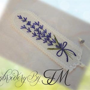 May include: Embroidered bookmark featuring a lavender sprig with purple flowers and green leaves, tied with a purple bow. The bookmark is white with a scalloped edge and the text "Embroidery By TM".