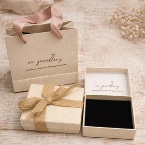 May include: A beige gift box tied with twine, a matching gift bag with pink handles, and an open jewellery box. The boxes and bag have the text "cc jewellery" and "meaningful pieces for the people you love."
