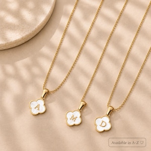 May include: Three gold-toned necklaces, each featuring a four-leaf clover pendant with a white inlay and a centred letter. The pendants display the letters A, M, and D respectively. The text Available in A-Z is printed in the bottom right corner.