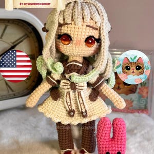 May include: A handcrafted crochet doll in a cream dress with brown details and a pink bunny. The doll features large eyes and the text "PDF PATTERN - YASIRO NENE - BY KITSUGURUMI CROCHET". The doll is a charming handmade item.