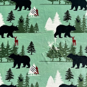 May include: A light green fabric with a repeating pattern of black bears, evergreen trees, and red deer. Some trees are white with red and black accents. The design evokes a forest theme.