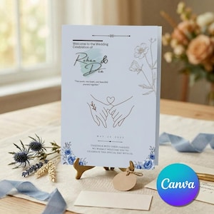 Può includere: Un cartello di benvenuto per matrimonio bianco con accenti floreali blu, un'illustrazione a linee di due mani unite da un cuore e il testo: Welcome to the Wedding Celebration of Rohan & Dia, Two souls, one heart, one beautiful journey together, May 26 2033.