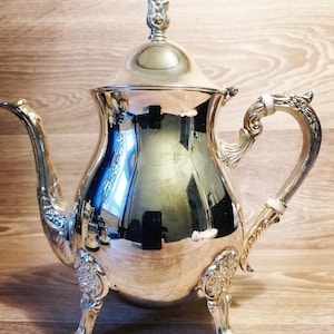 以下が含まれることがあります： 装飾的なディテールが施された銀色のティーポット。 ティーポットは、湾曲した注ぎ口、装飾的なハンドルを備え、3つの小さな足の上に置かれています。 蓋には装飾的なつまみが付いています。 ティーポットは非常に反射性があります。