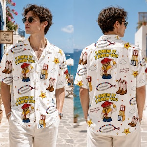 May include: A white short-sleeved button-down shirt featuring a repeating graphic print of a cowgirl, cowboy boots, yellow sheriff stars, alphabet blocks labeled T, S, 5, and the text I KNEW IT I KNEW YOU with a collar and front buttons.