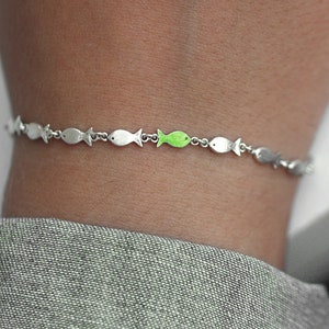 Simmar mot strömmen. Fiskstim med en grön emaljerad fisk som simmar mot strömmen. Unika smycken för henne.