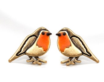 May include: A pair of gold-tone earrings featuring a robin design. The robins are orange, black, and white.