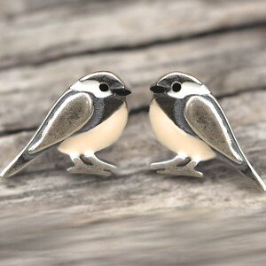 Puede incluir: Un par de pendientes de plata en forma de p&aacute;jaro con ojos negros y alas blancas y grises. Los p&aacute;jaros se miran.