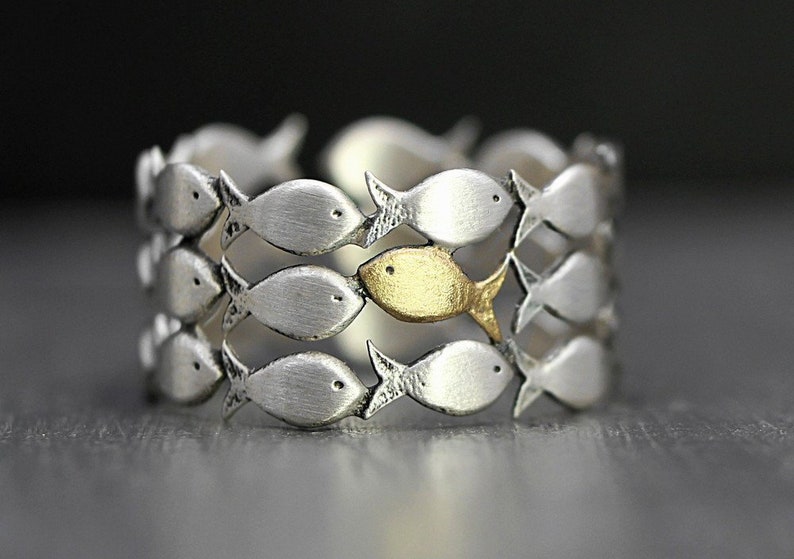 May include: A silver ring with a school of fish design. One fish is gold, while the rest are silver.