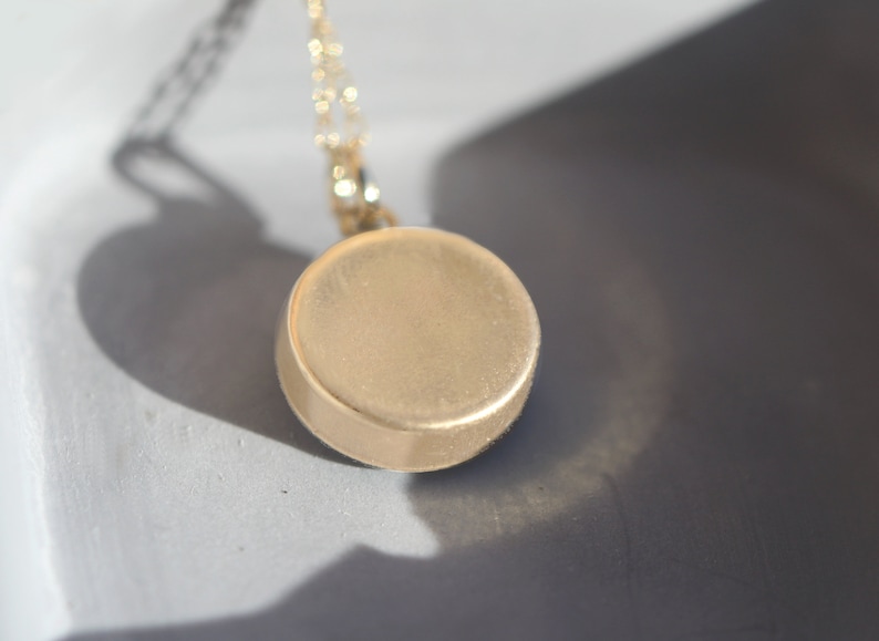 K&ouml;nnte beinhalten: Eine goldene Halskette mit einem runden Anh&auml;nger. Der Anh&auml;nger ist glatt und hat eine gl&auml;nzende Oberfl&auml;che.