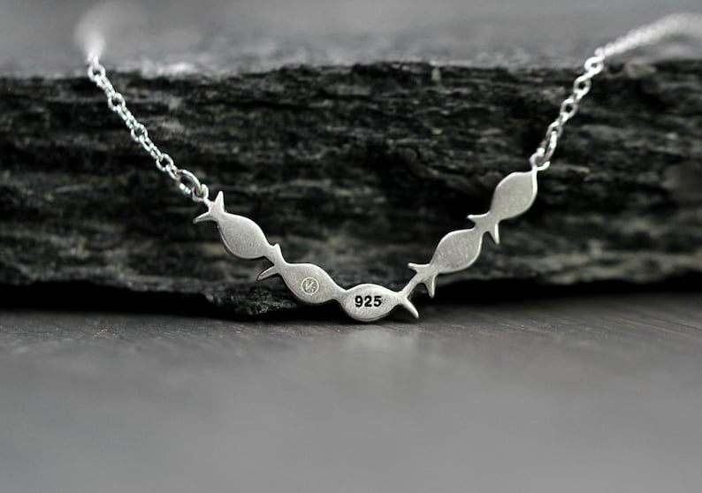 May include: Silver necklace with a chain and a pendant of five fish in a row. The pendant is stamped with "925" on the back.