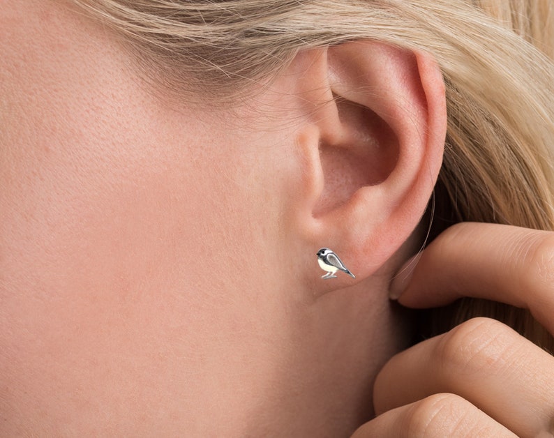 Puede incluir: Un par de pendientes de bot&oacute;n de plata con un peque&ntilde;o dise&ntilde;o de p&aacute;jaro carbonero detallado.