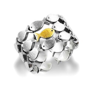 May include: A silver ring with a design of a school of fish. One fish is gold and the rest are silver.