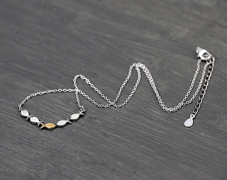 May include: A silver chain necklace with a pendant of small silver fish, one of which is gold. The necklace has an adjustable length.