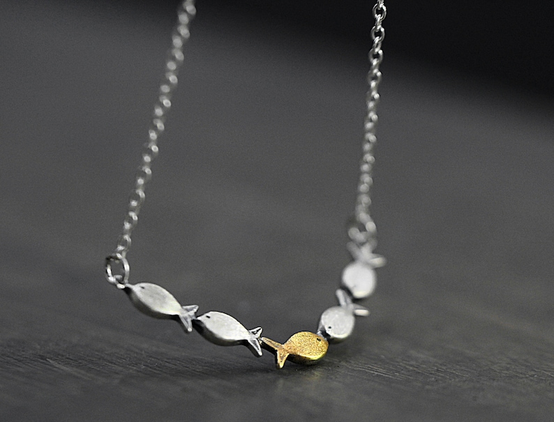 May include: A silver chain necklace with a pendant of five silver fish, one of which is gold.