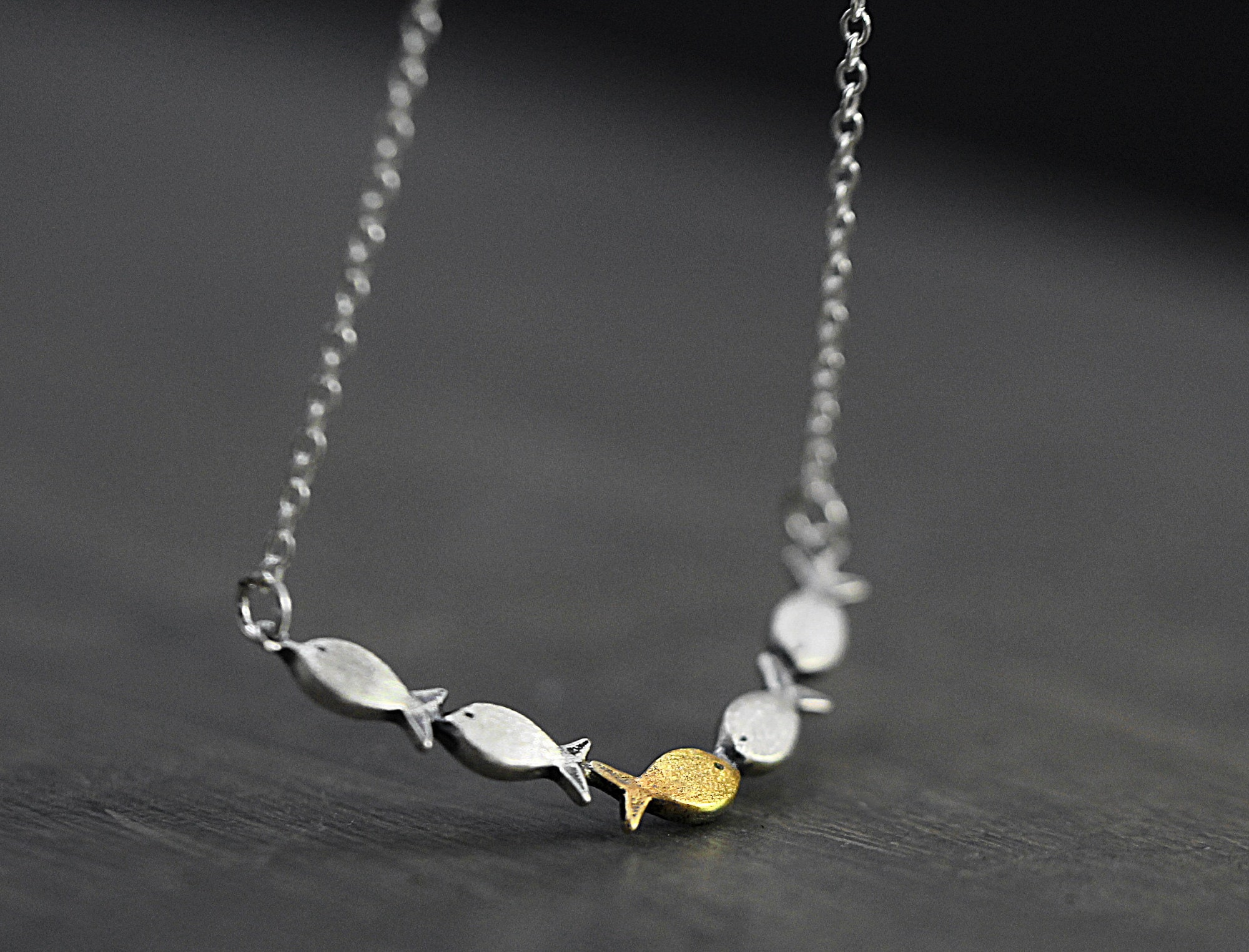 Swimming against the current. Dainty silver necklace. School of fish with one golden enameled fish swimming upstream. Gift for her.