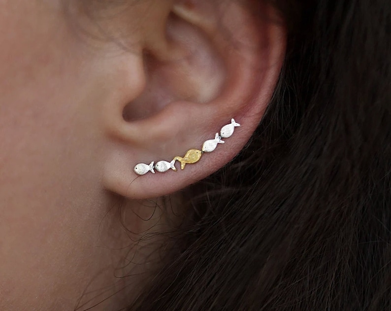 May include: A silver and gold fish ear crawler earring. The earring is made up of a row of small fish charms, with the fish alternating between silver and gold.
