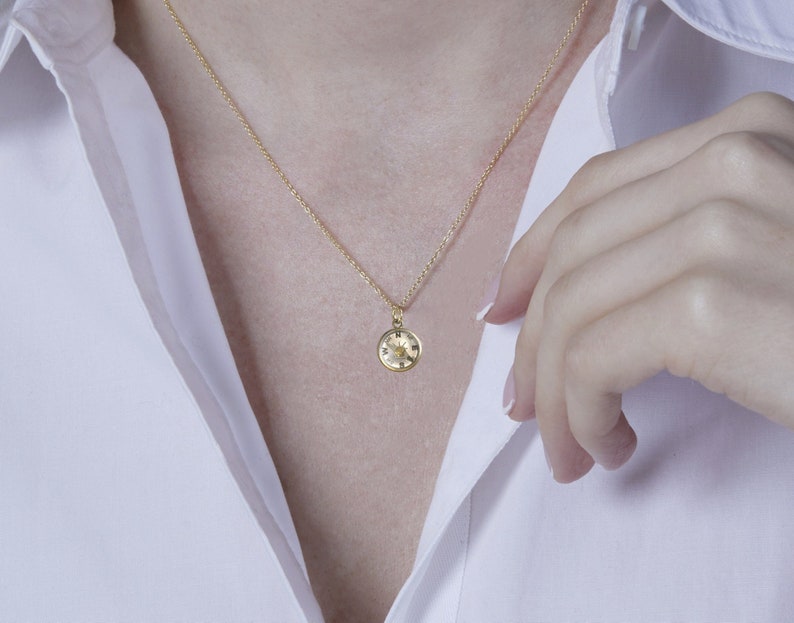 K&ouml;nnte beinhalten: Eine goldene Kettenkette mit einem kleinen runden Anh&auml;nger mit Kompass-Design.