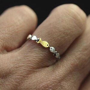 May include: A silver ring with a row of small fish charms. Some of the fish are gold and some are silver.