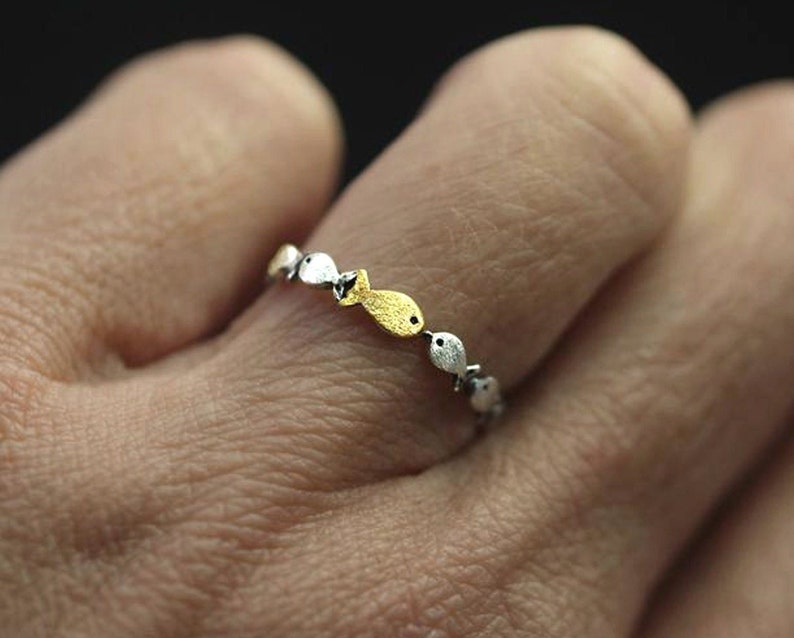 May include: A silver ring with a row of small fish charms. Some of the fish are gold and some are silver.