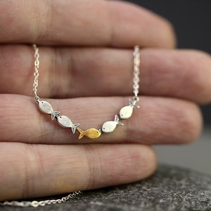 May include: A silver chain necklace with a row of small silver and gold fish charms. The fish are facing the same direction and are arranged in a curved line.