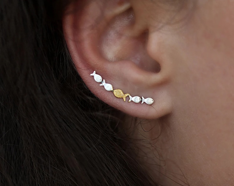 May include: A silver and gold fish ear crawler earring. The earring is made up of a line of small fish, alternating between silver and gold.