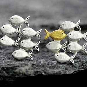 May include: A pair of silver fish earrings, one with a gold fish in the center. The fish are arranged in a school formation.