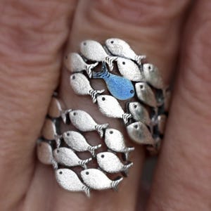 Könnte beinhalten: Ein silberner Ring mit einem Design aus einem Schwarm Fische. Ein Fisch ist blau, während die anderen silberfarben sind.
