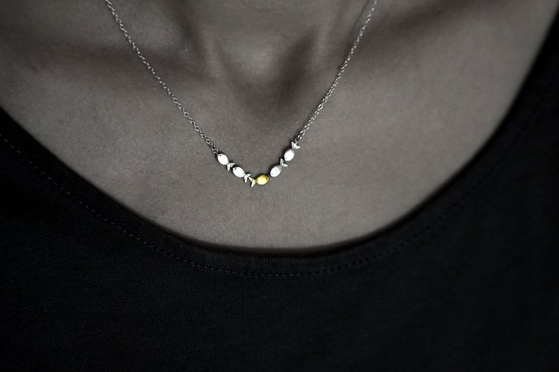 May include: A silver necklace with a row of small silver fish charms, with a single gold fish charm in the center.