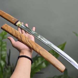 May include: A straight-bladed sword with a polished silver-colored metal blade and a wooden handle. The sword is accompanied by a matching wooden scabbard featuring a distinct wood grain pattern, with a brass-colored collar at the blade base.