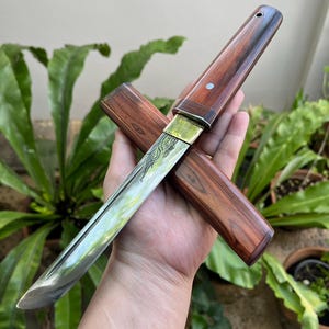 May include: A white-painted wooden 'Welcome' sign with a distressed finish, featuring a floral design in pink and green. The sign is designed for hanging and is crafted by hand. The text is in a whimsical font, suitable for a door or wall.