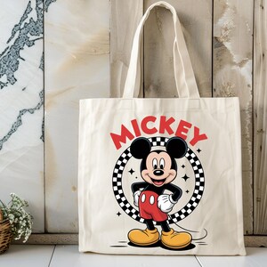 May include: A cream-colored canvas tote bag featuring a graphic of Mickey Mouse standing inside a black and white checkered circle. The word MICKEY is printed in bold red letters above the circle, and small four-pointed star accents surround the character.