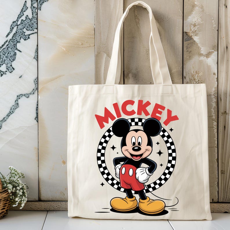 May include: A cream-colored canvas tote bag featuring a graphic of Mickey Mouse standing inside a black and white checkered circle. The word MICKEY is printed in bold red letters above the circle, and small four-pointed star accents surround the character.