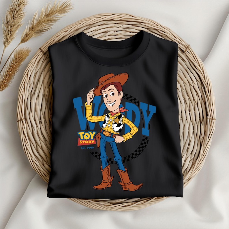 May include: Black t-shirt featuring a cartoon illustration of Woody from Toy Story. Woody is wearing a cowboy hat, vest, and boots. The shirt has the text "WOODY" and "TOY STORY EST. 1995".