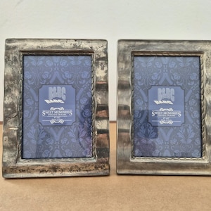 Könnte beinhalten: Zwei silberfarbene Fotorahmen mit strukturierten Kanten. Jeder Rahmen enthält einen blauen Einsatz mit dem Text "Sweet Memories Photo Frame". Die Rahmen sind rechteckig und stehen nebeneinander auf einer hellbraunen Oberfläche.