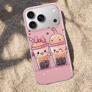Può includere: Custodia per telefono rosa con un'illustrazione a cartoni animati di due bevande al tè alle bolle sorridenti. Le bevande hanno perle di boba marroni, fiocchi rosa e cannucce. La custodia è su una superficie sabbiosa.