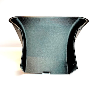 以下が含まれることがあります： 黒いプラスチック製の自動車部品で、表面はテクスチャ加工されています。 上部は湾曲し、側面はフレア状になっており、下部に小さな長方形の切り欠きがあります。 車両のインテリアに組み込むように設計されています。