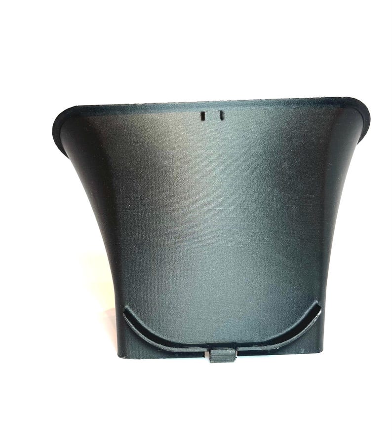 以下が含まれることがあります： 黒色の漏斗型のオブジェクトで、表面はざらざらしています。上部に幅広の湾曲した開口部があり、下部に狭い湾曲した開口部があります。上端近くに2つの小さな長方形の穴が見えます。オブジェクトはプラスチック製のように見えます。