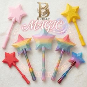 Puede incluir: Una colección de varitas mágicas en forma de estrella en varios colores, incluyendo rosa, rojo, amarillo, azul y arcoíris. Las varitas tienen un diseño facetado y están dispuestas sobre un fondo claro. La palabra "MAGIC" está escrita en cursiva.